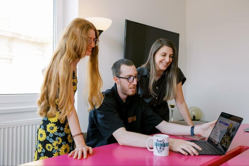 Three Wolfpack Digital team members looking at a laptop together at a pink desk